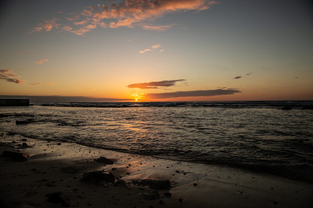 The sun is setting over a beach with rocks and water.