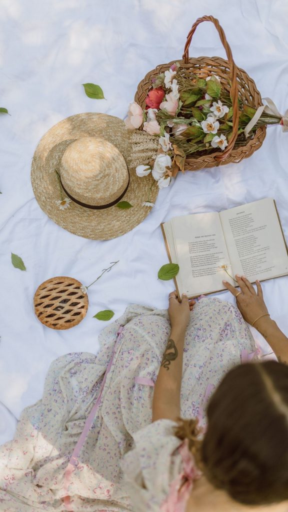 Photo of woman in cottagecore dress having a picnic outside and reading a book