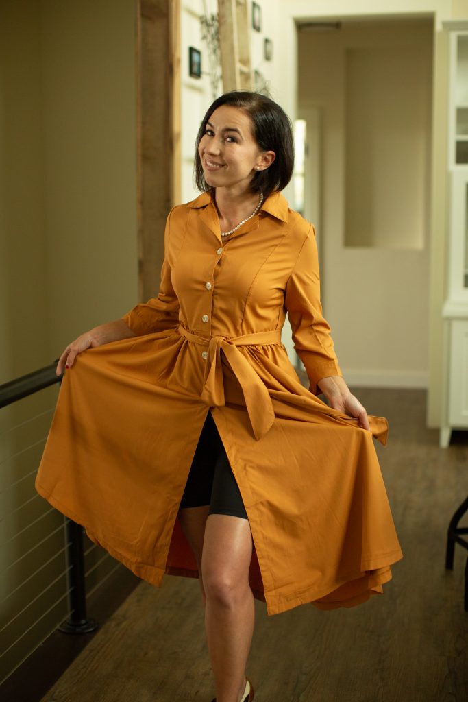 A woman poses wearing a long orange dress that buttons up the front, showing the black bike shorts she's wearing under the dress.