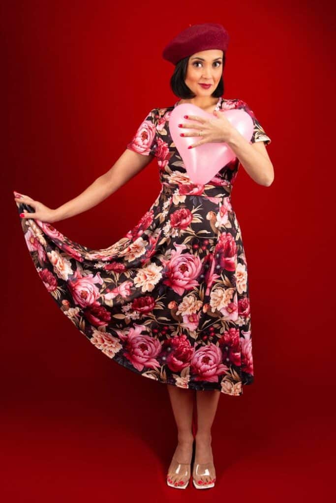 A woman holding a pink heart balloon and wearing a red beret and the Lyra Dress - Romantic Floral