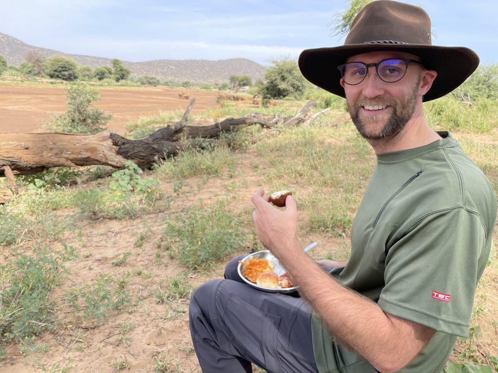 A man in a hat eating a plate of food during a safari.