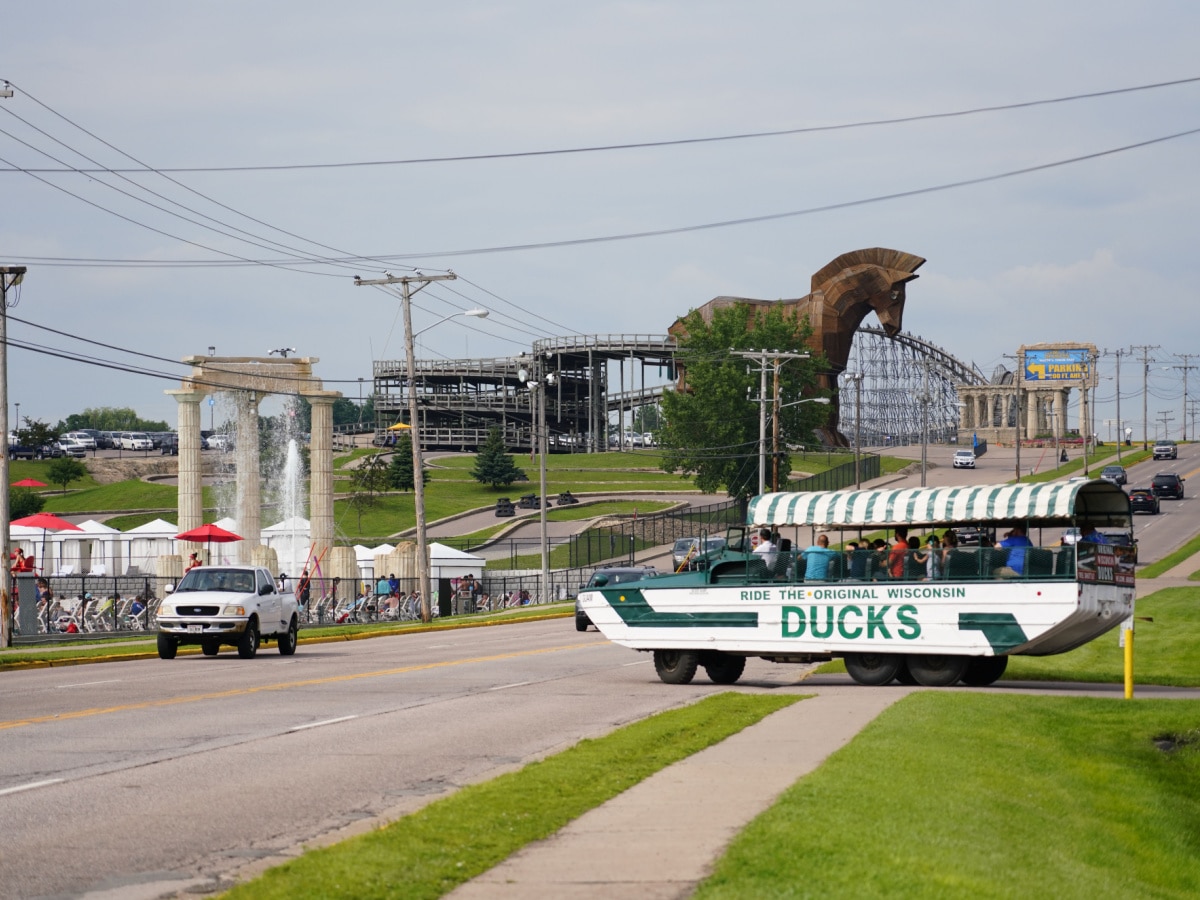 An Original Wisconsin Ducks vehicle pulls out onto the main highway road in the Wisconsin Dells, taking visitors on a land and lake scenic tour. In the background is the Trojan Horse structure at Mt. Olympus adventure park.