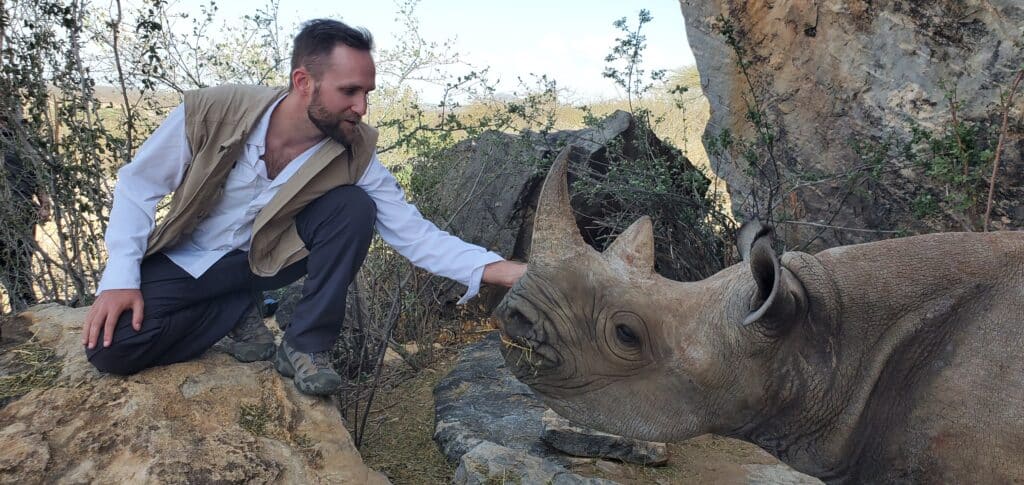 Zac wearing a SCOTTeVEST vest and Prana pants petting a rhino