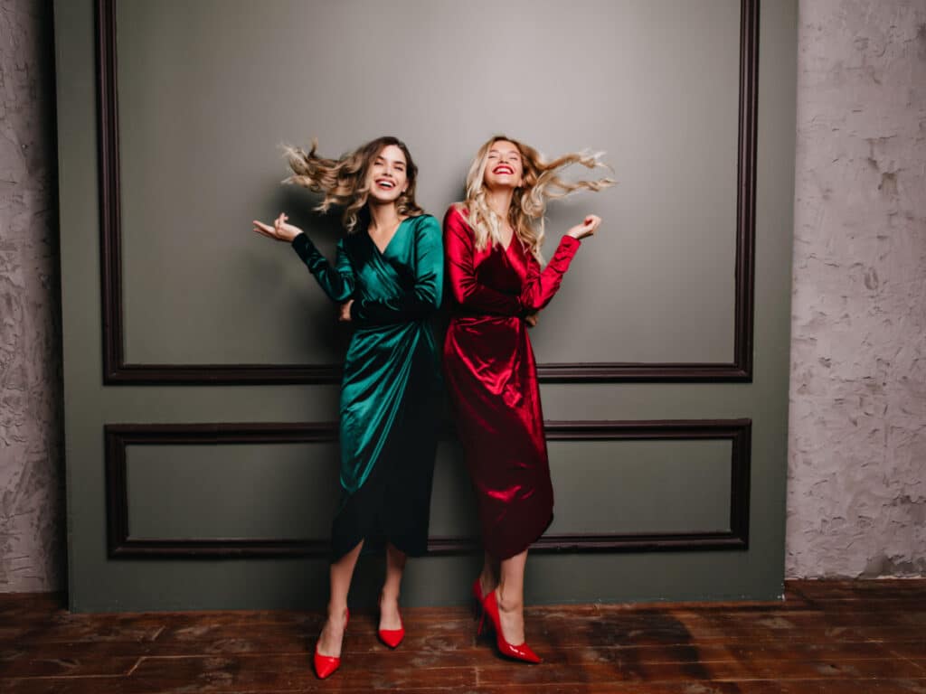 Full-length portrait of smiling girls wears long dresses and red shoes. Studio photo of good-looking female models in velvet clothes.