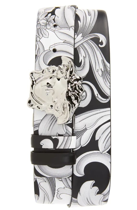 A black and white floral belt with a silver buckle on a white background.