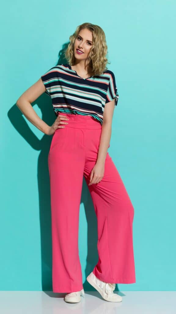 A woman in pink wide leg pants posing against a blue wall.