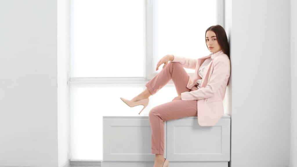 A woman in a pink suit sitting in front of a window.