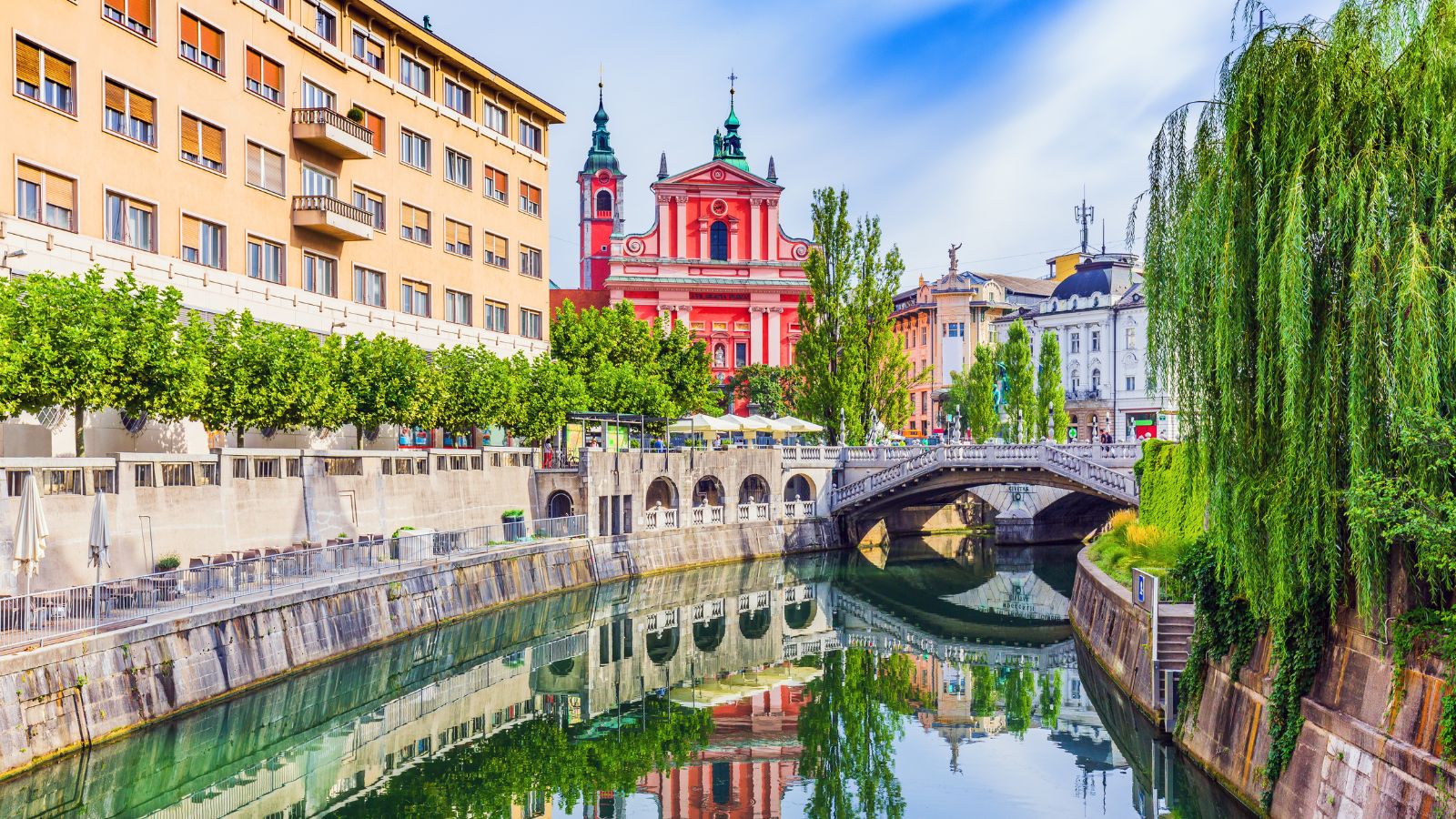 A picturesque look at the city of Ljubljana, Slovenia along the river. Calm waters reflect the colorful buildings and trees that line the canal.