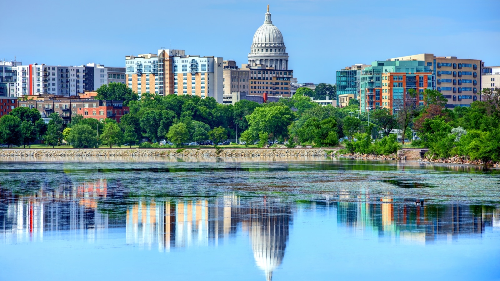 A view of downtown Madison from across the lake. The dome of the Wisconsin state capitol building is visible between residential buildings and offices.