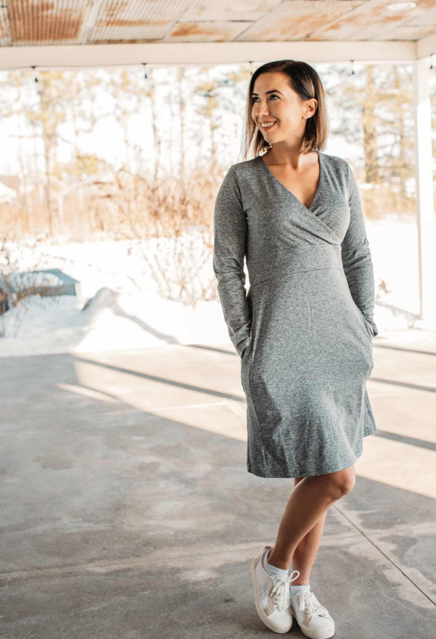 Lindsay poses outdoors on a sunny winter day. She's wearing a casual knee-length gray dress and white sneakers.