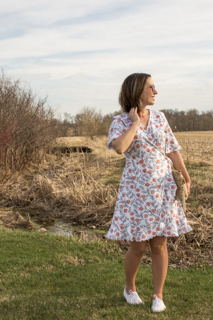 Lindsey of Have Clothes, Will Travel wearing a floral Passion Lilie summer wrap dress with a field and stream as a backdrop