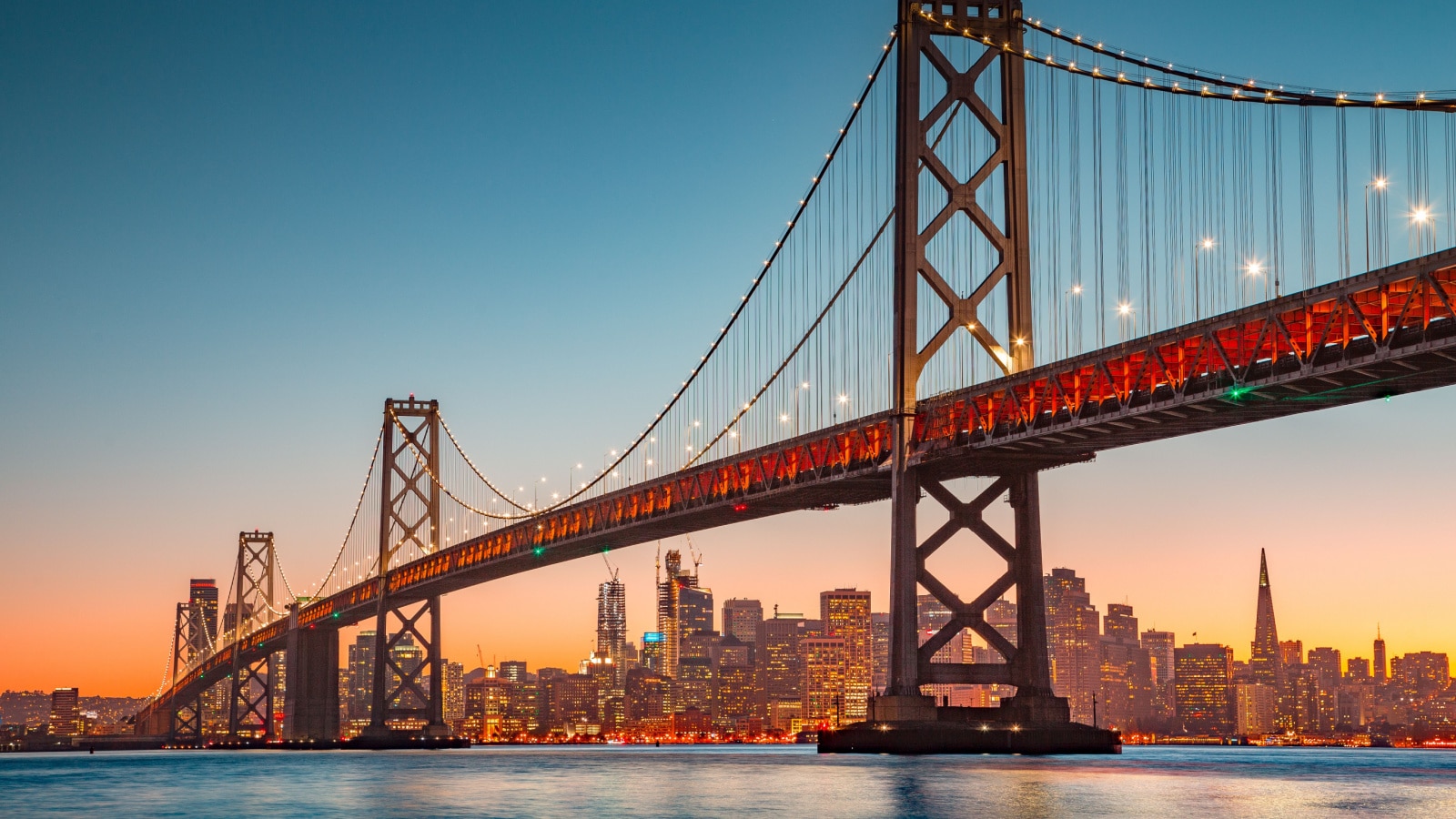 Classic panoramic view of San Francisco skyline with famous Oakland Bay Bridge illuminated in beautiful golden evening light at sunset in summer, San Francisco Bay Area, California, USA