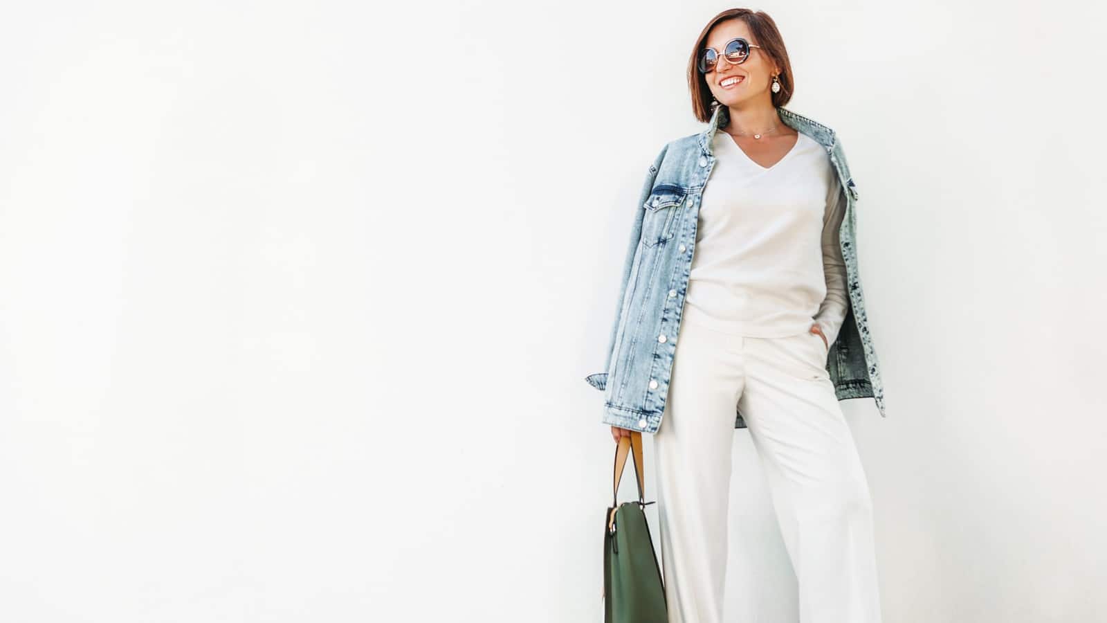 Posing woman in elegant white outfit with oversize denim jacket