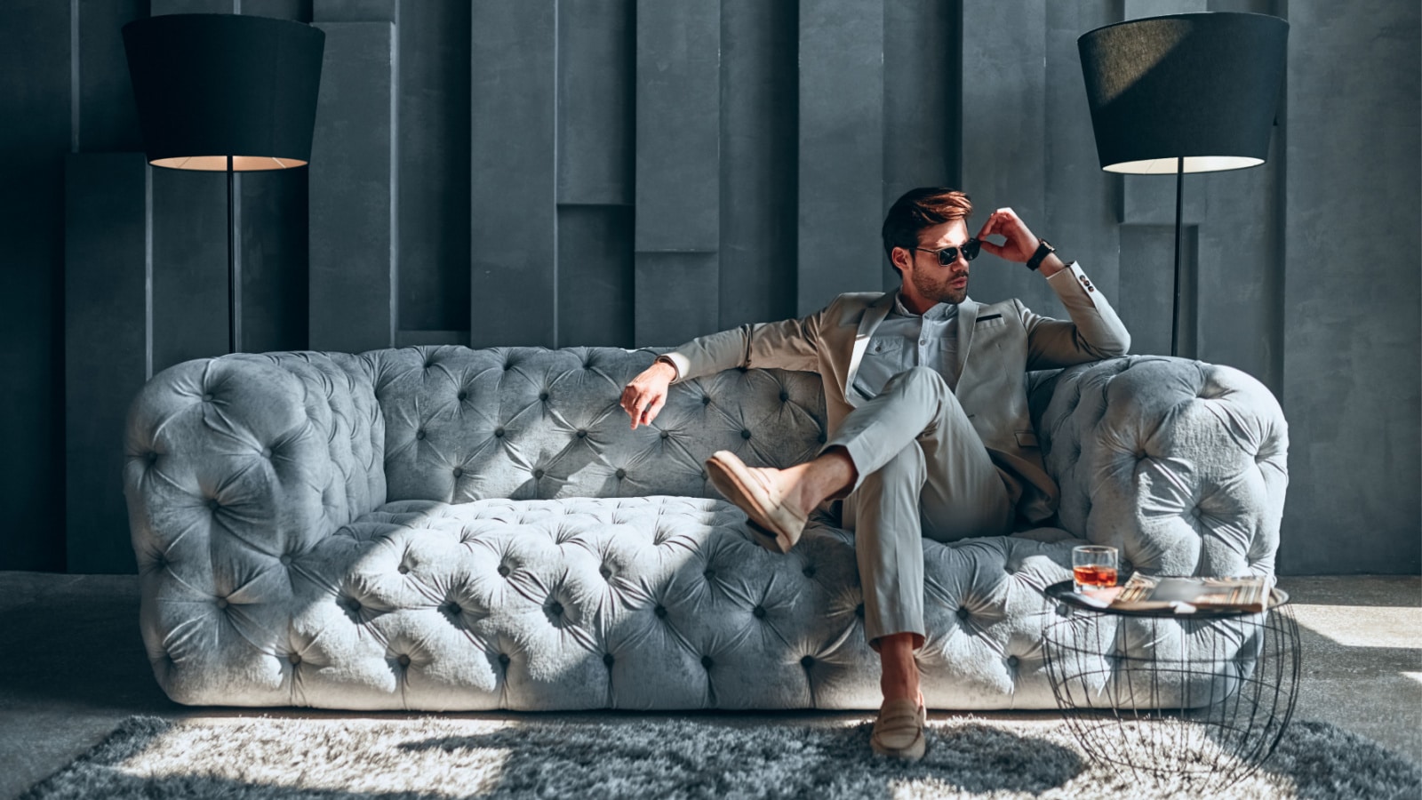 Handsome stylish man in beige suit at home sitting on sofa.