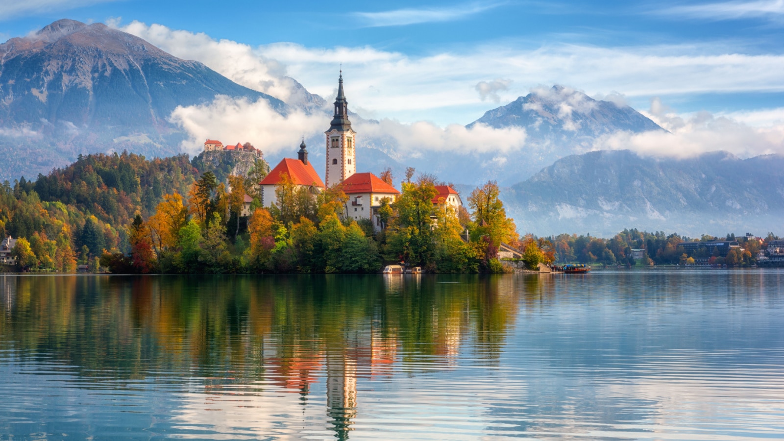 Famous alpine Bled lake (Blejsko jezero) in Slovenia, amazing autumn landscape. Scenic view of the lake, island with church, Bled castle, mountains and blue sky with clouds, outdoor travel background