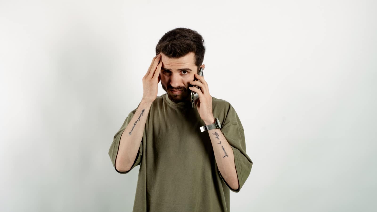 Handsome young man wearing casual clothes posing isolated over white background feeling upset desperate talking on the phone having problems. Hearing bad news during mobile conversation.