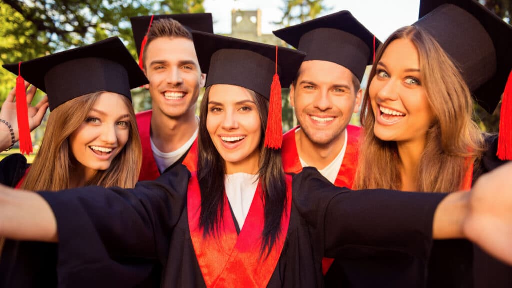 excited five successful happy five graduates in robes and hats with tassel together making selfie photo.