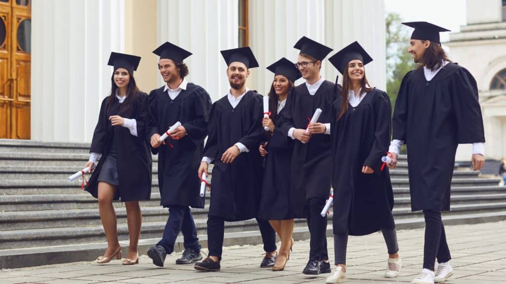 Successful graduates in academic dresses are walking and talking outdoors