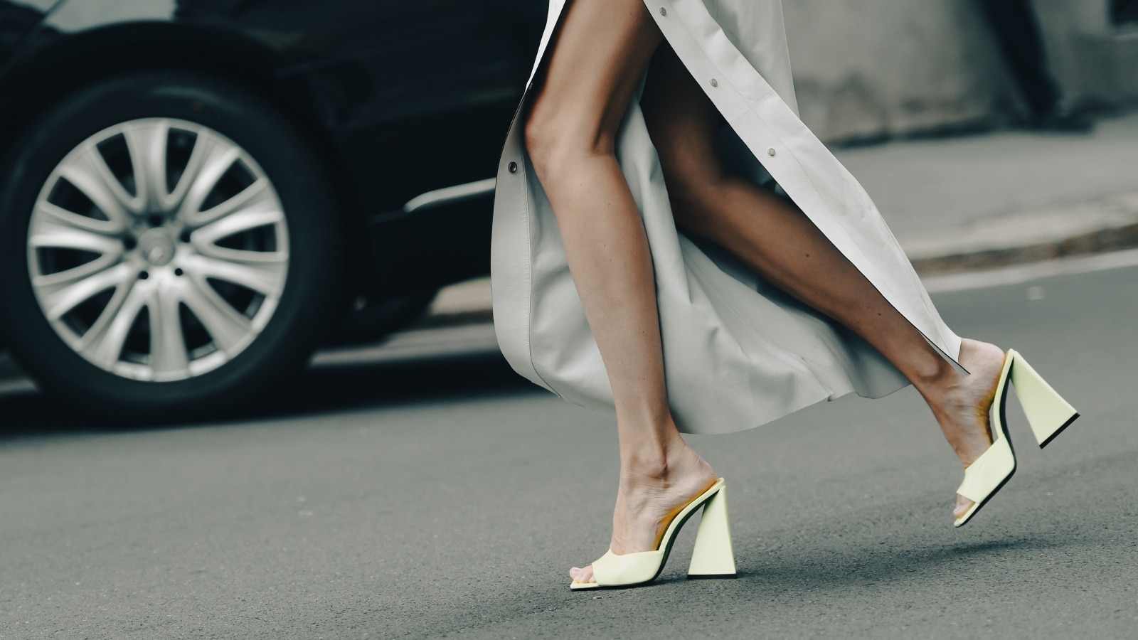 Milan, Italy - September 24, 2021: Street style outfit, fashionable woman wearing a pale gray shiny leather split long skirt, neon yellow shiny leather open toe-cap block heels shoes in Milan, Italy.