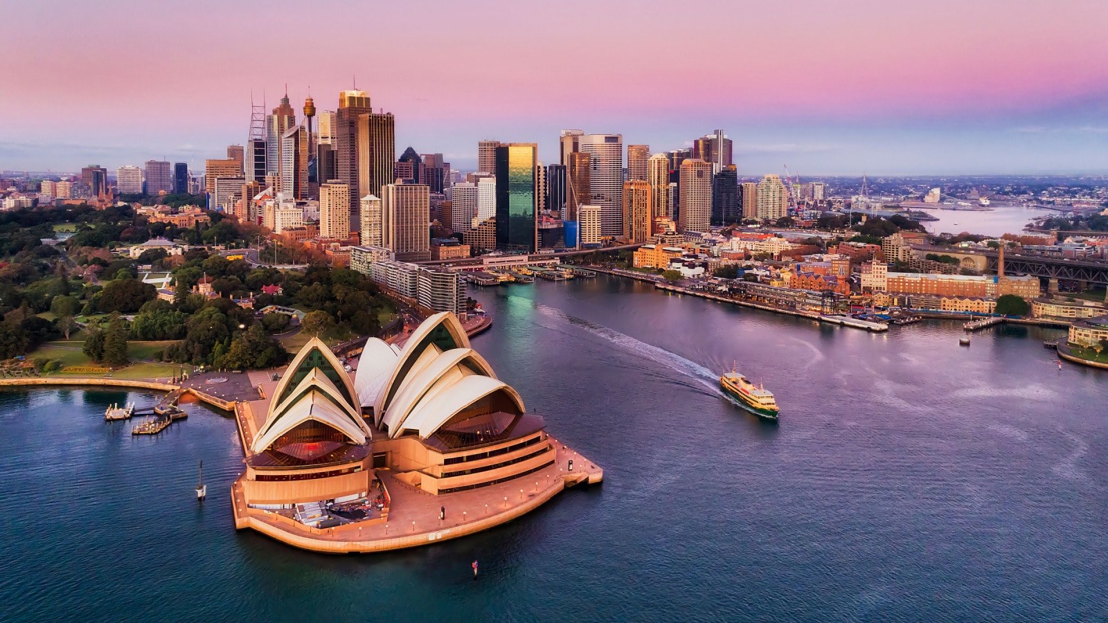 Pinkish colourful sunrise over Sydney city CBD on waterfront of Harbour around Circular quay with major architectural landmarks and symbols of Australia.