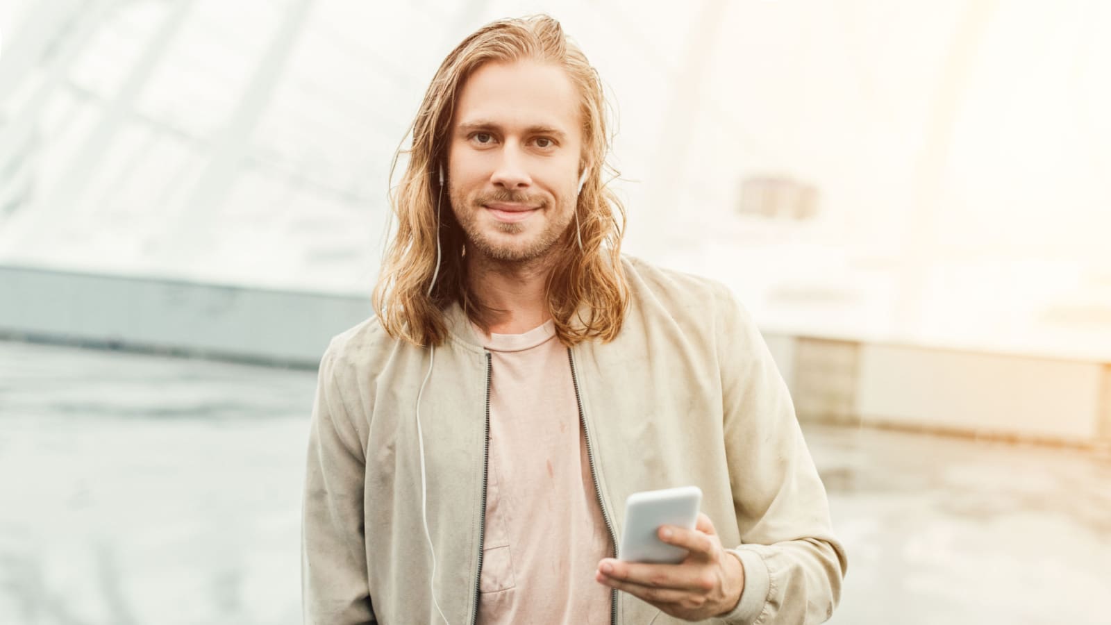 happy young man listening music with earphones and smartphone on street and looking at camera