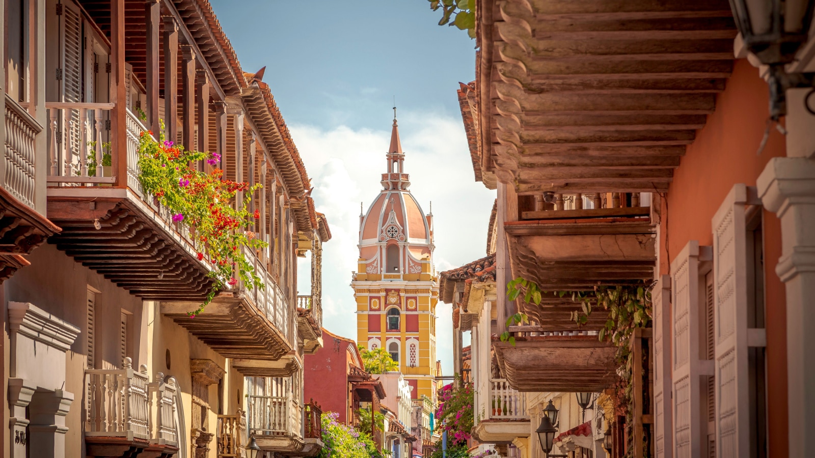 An image of Cartagena de Indias - the walled city - in Colombia. The dome of the building is seen from a city street, lined with homes and balconies decorated with flowers.