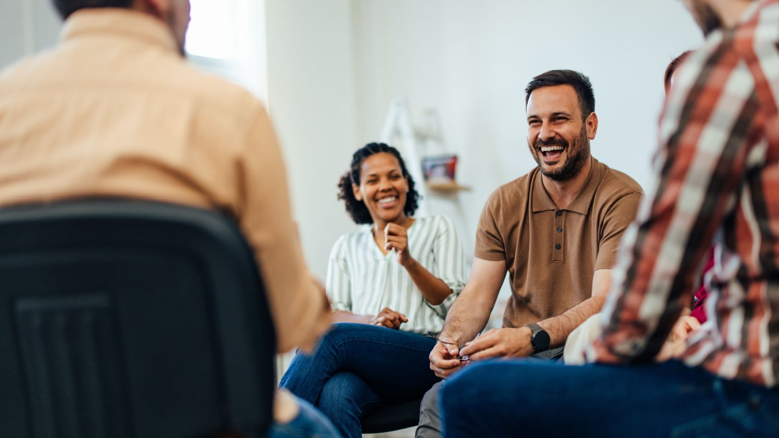 Focus on the smiling man, talking with people of all ages, during the group therapy.