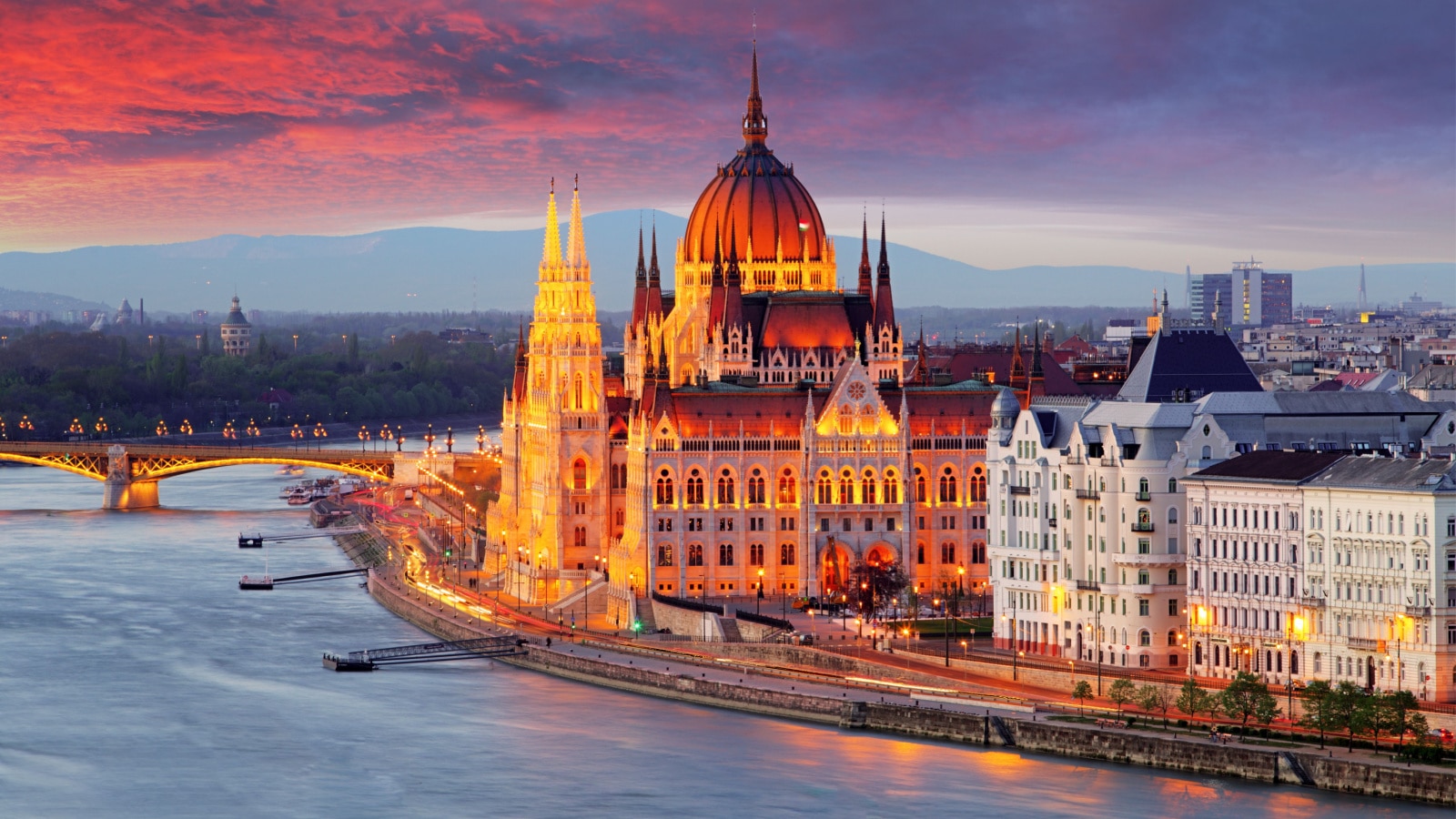 An aerial view of the Hungarian parliament building in Budapest, warmly lit in Amber light at sunset.