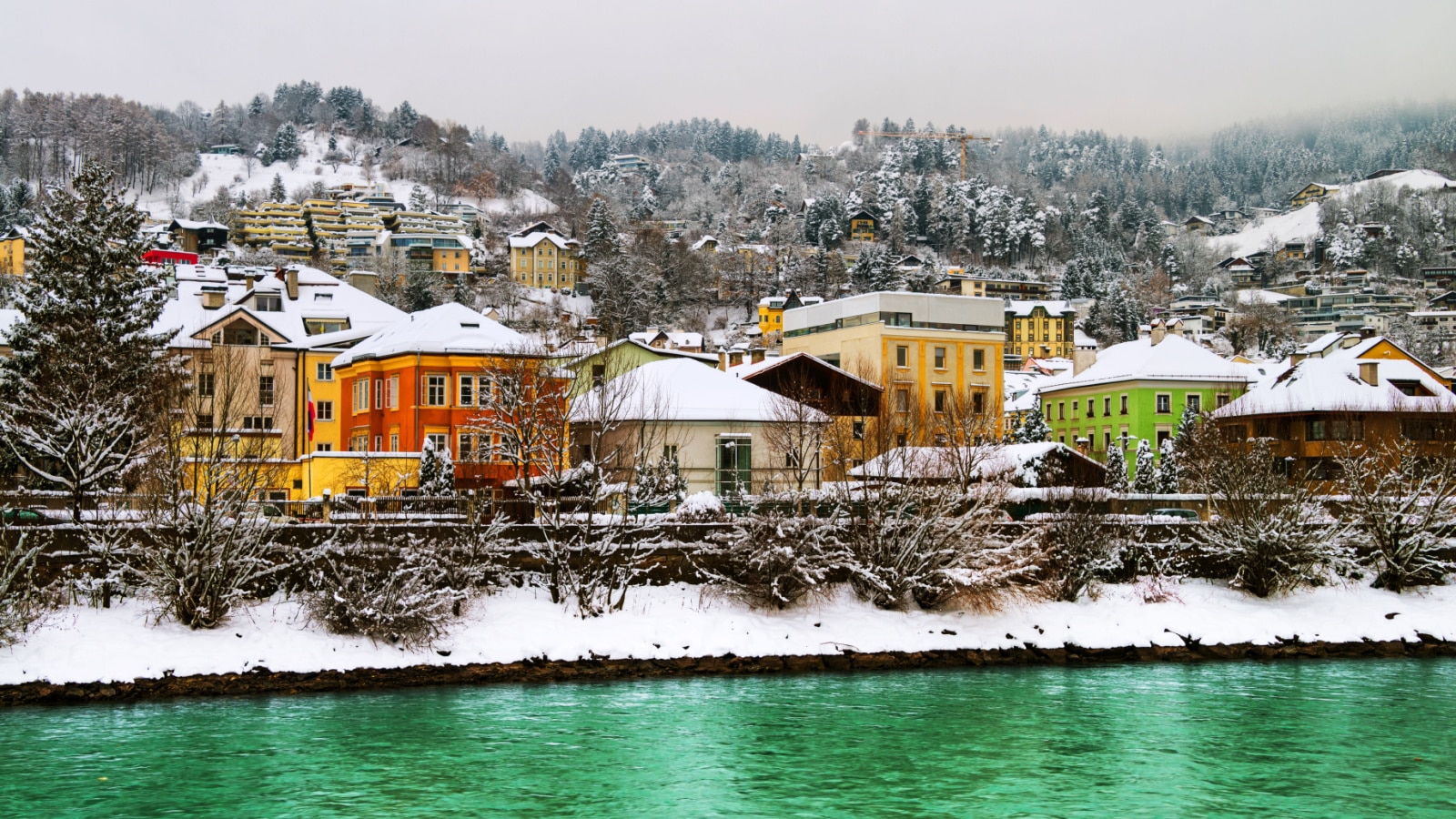 Innsbruck, Austria. View of the Inn river in winter in Innsbruck, Austria during the early morning, trees and mountains at the background. Various hotels and restaurants