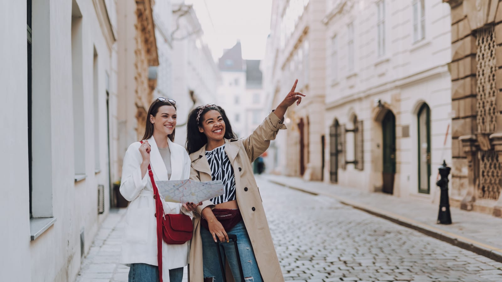 Attractive afro american lady pointing at something interesting while her friend holding city map and smiling