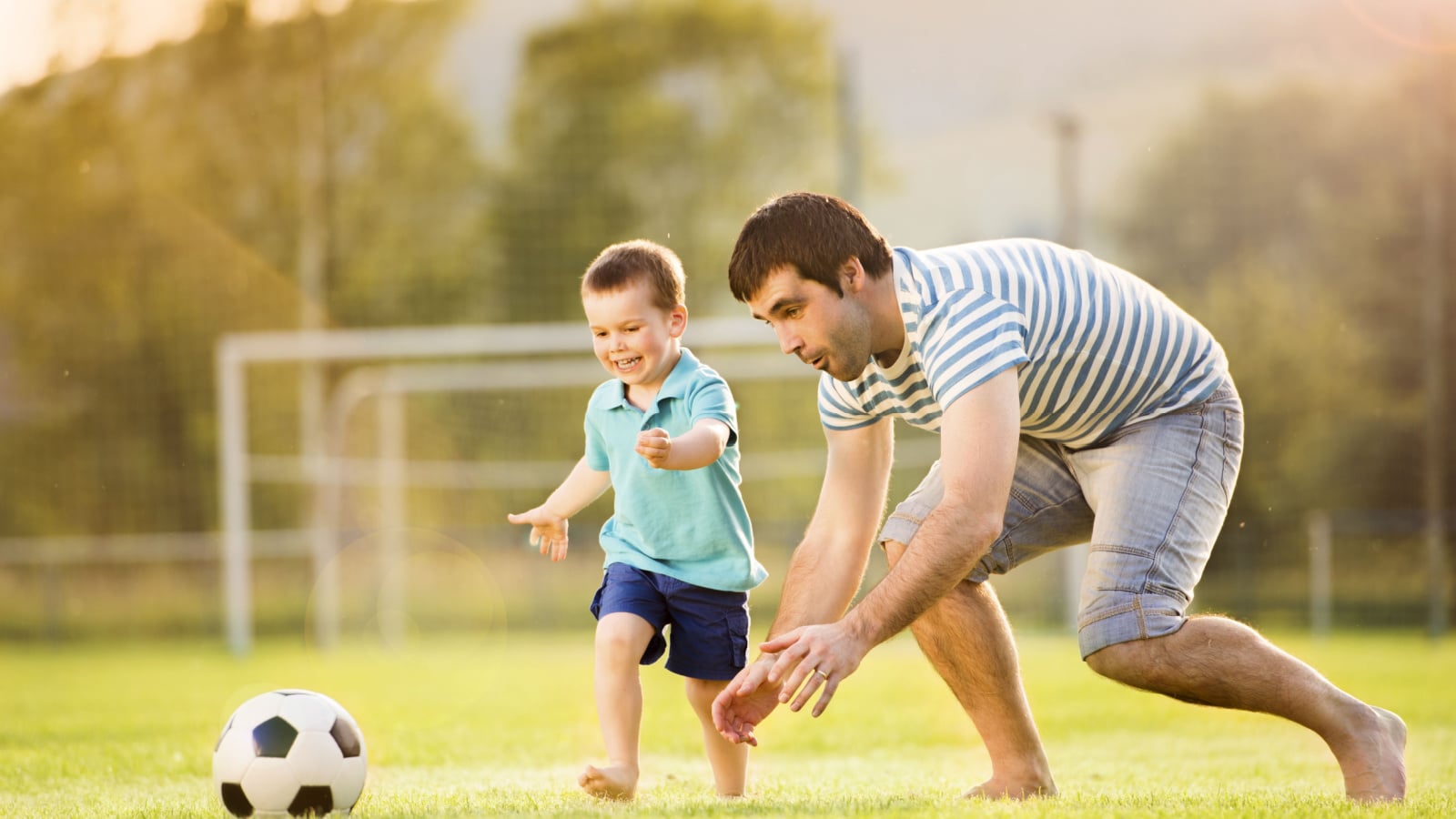 Young father with his little son playing football on football pitch