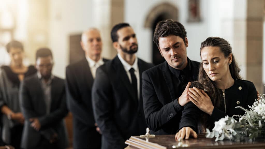 Death, funeral and family touching coffin in a church, sad and unhappy while gathering to say farewell. Church service casket and sad man and woman looking upset while greeting, goodbye and rip