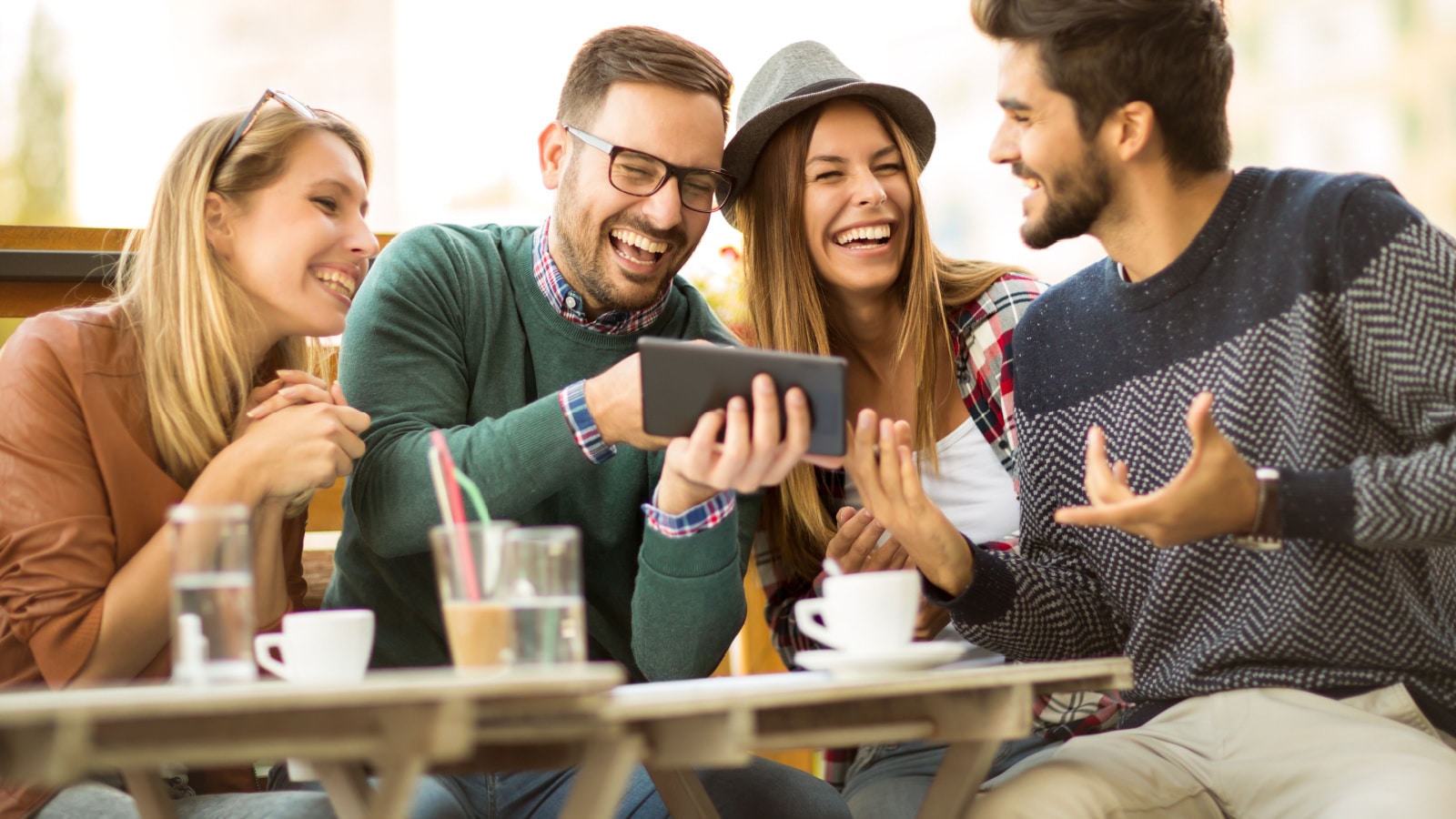 Group of four friends having a coffee together. Two women and two men at cafe talking laughing and enjoying their time using digital tablet.