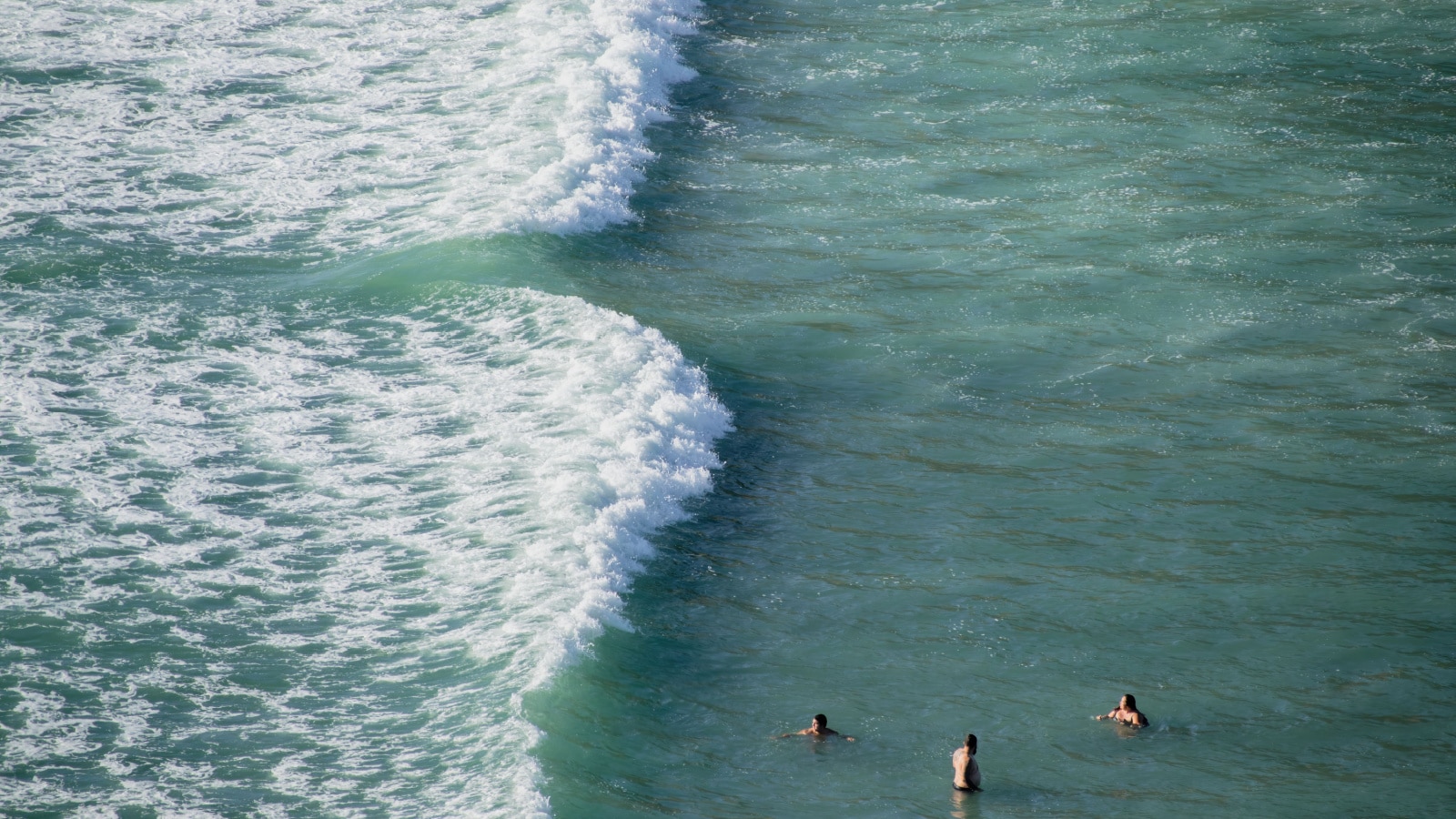 View of three tourists bathing near dangerous rip current at Piha beach, Auckland, New Zealand. Auckland, New Zealand - February 21, 2021