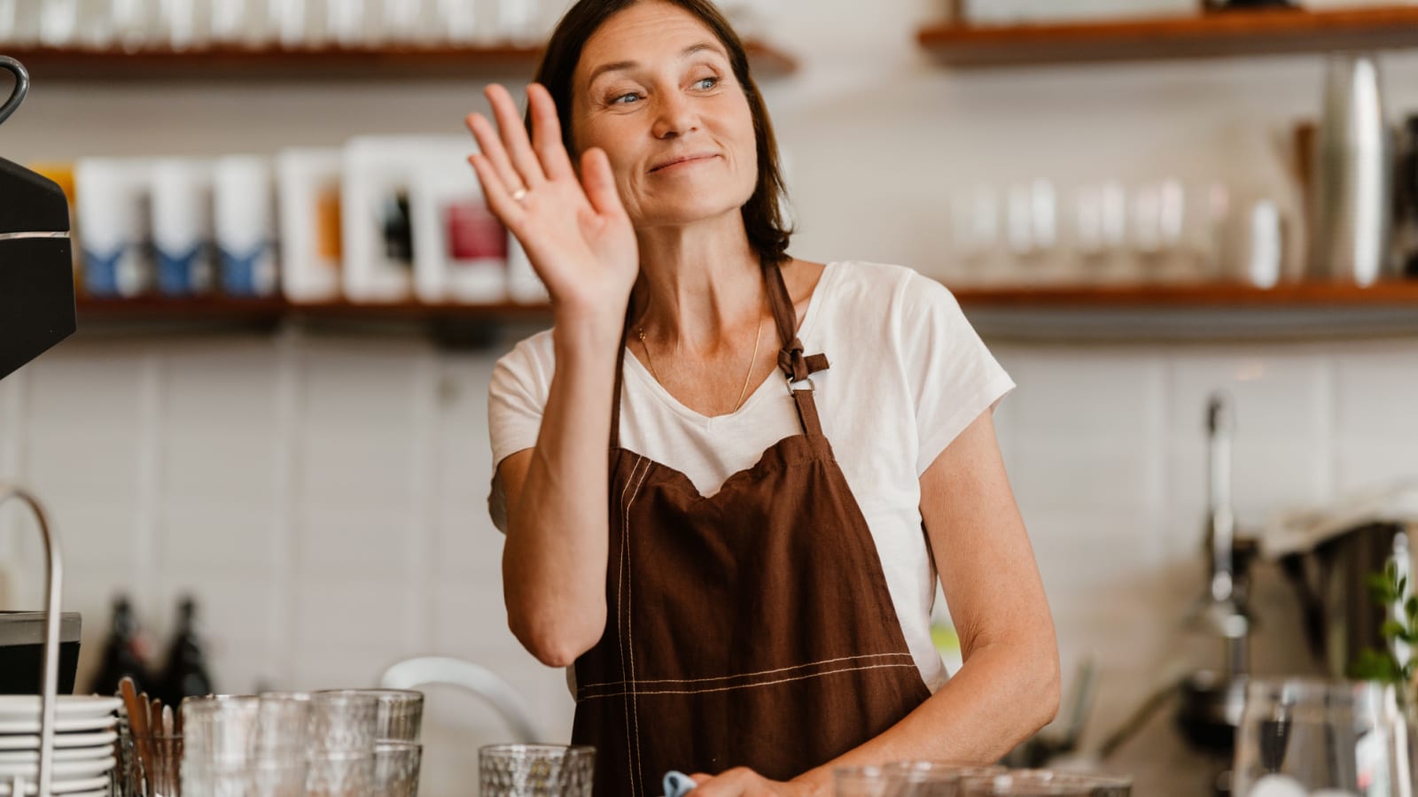 White mature barista woman smiling and welcoming customers while working in cafe indoors