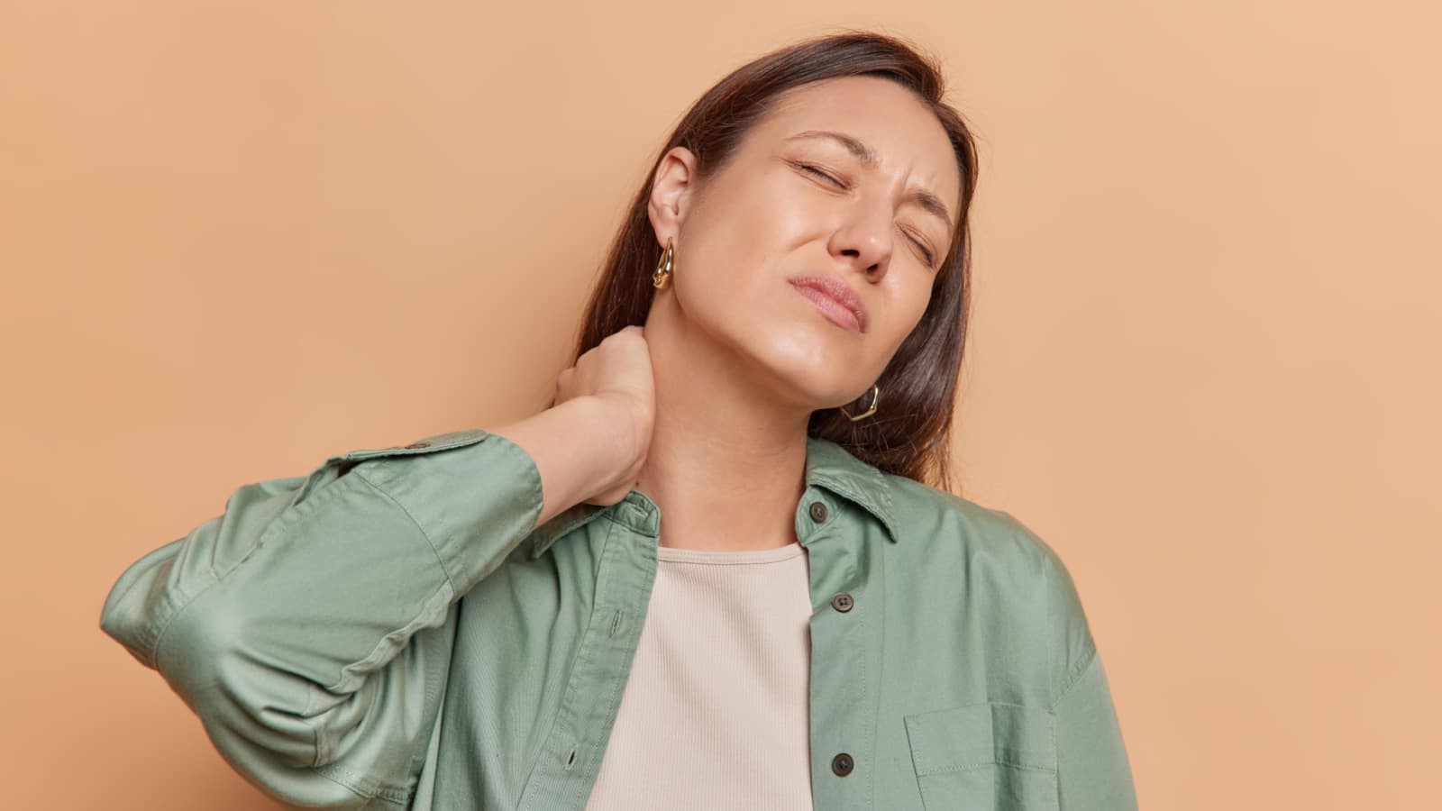 Young woman touches neck feels physical discomfort massages tensed muscles relieves joint shoulder ache keeps eyes closed feels fatigue after working in garden isolated over brown background