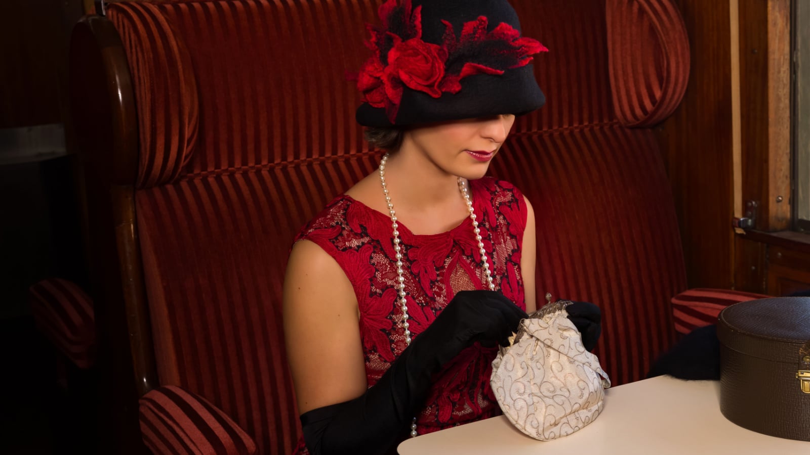 Attractive 1920s woman in red flapper dress and cloche hat posing in the 1927 first class interior of an authentic steam train