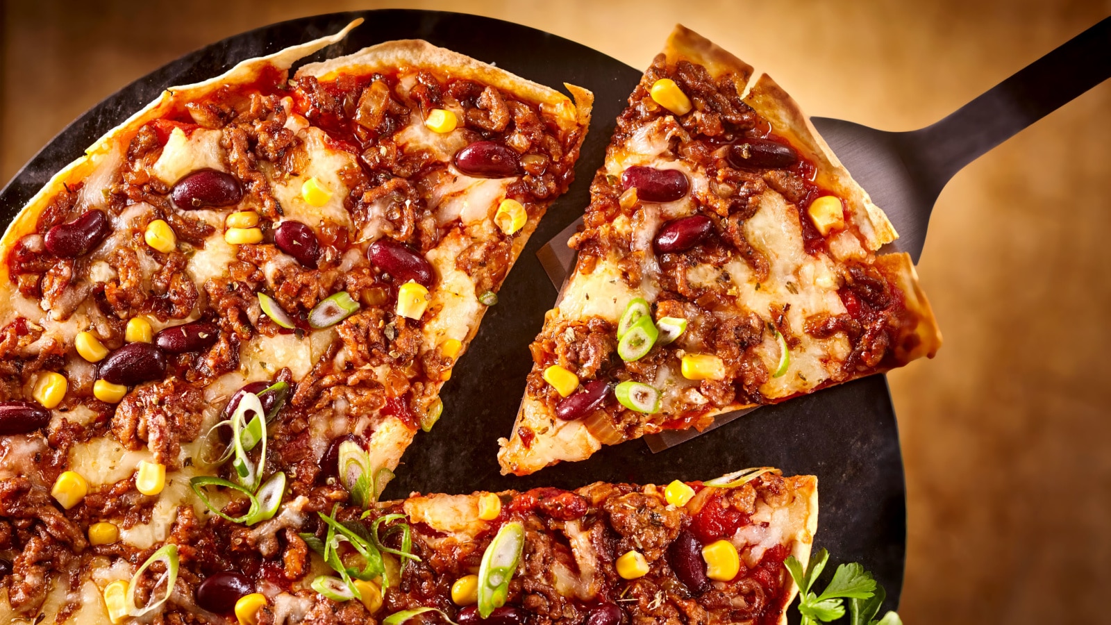 Top down view on spatula holding triangular slice of bean and cheese pizza for Tex-Mex theme meal