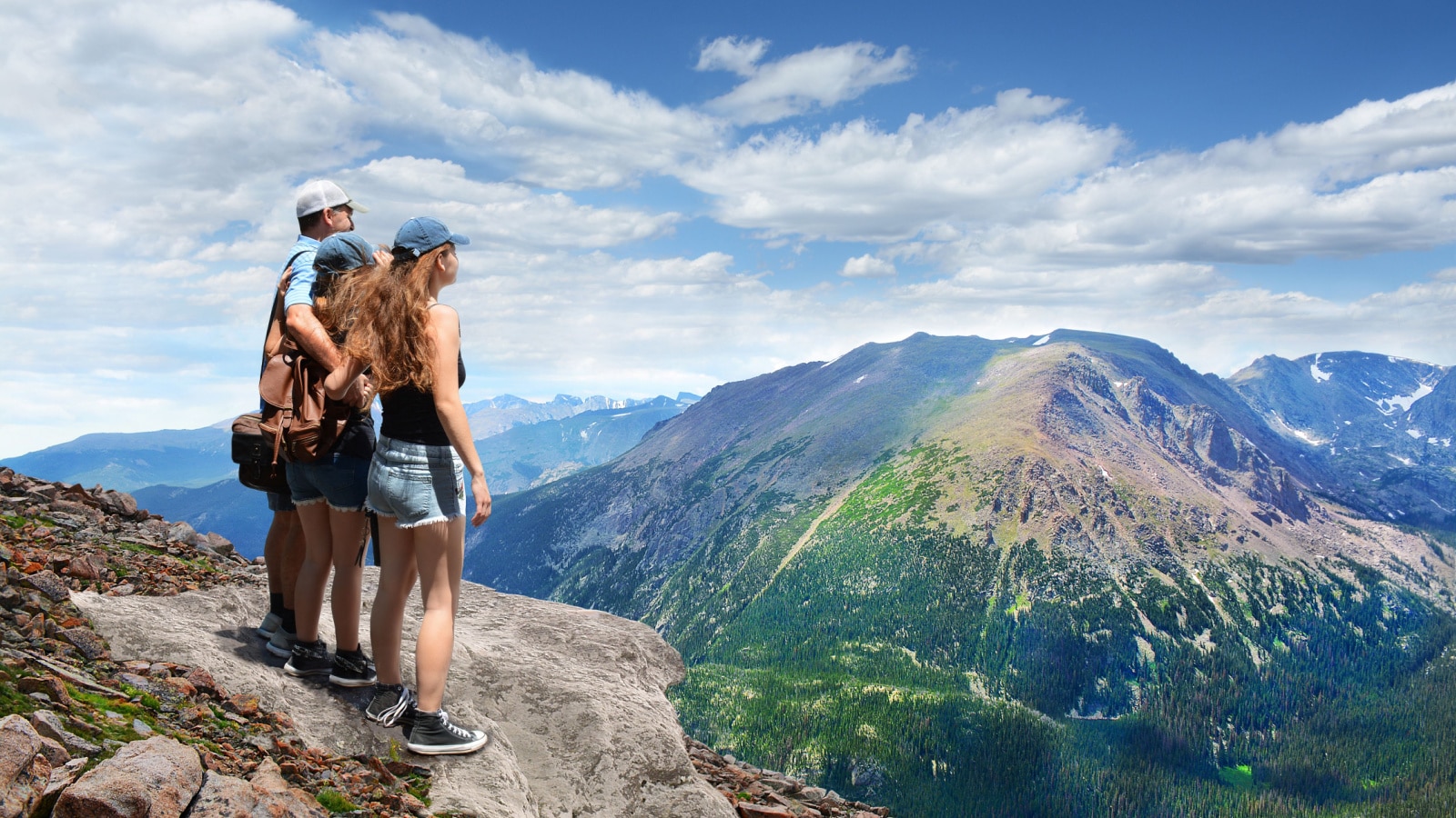 Father with arms around his family looking at summer mountains landscape, on hiking trip, on top of mountain. View from Trail Ridge Road. Estes Park, Rocky Mountains National Park, Colorado.