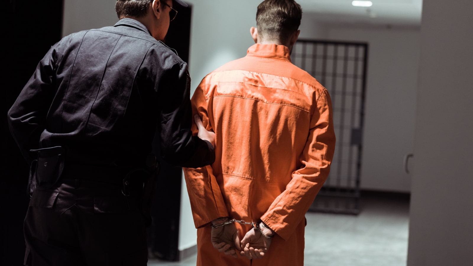 rear view of prison officer leading prisoner in handcuffs in corridor