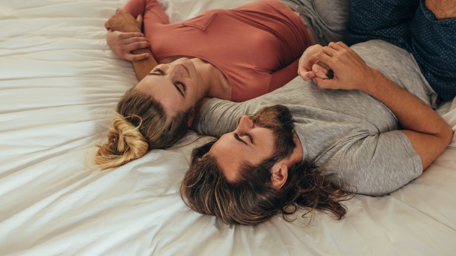 Romantic couple lying on bed holding hands and talking. Woman sleeping on arm of her husband on bed.