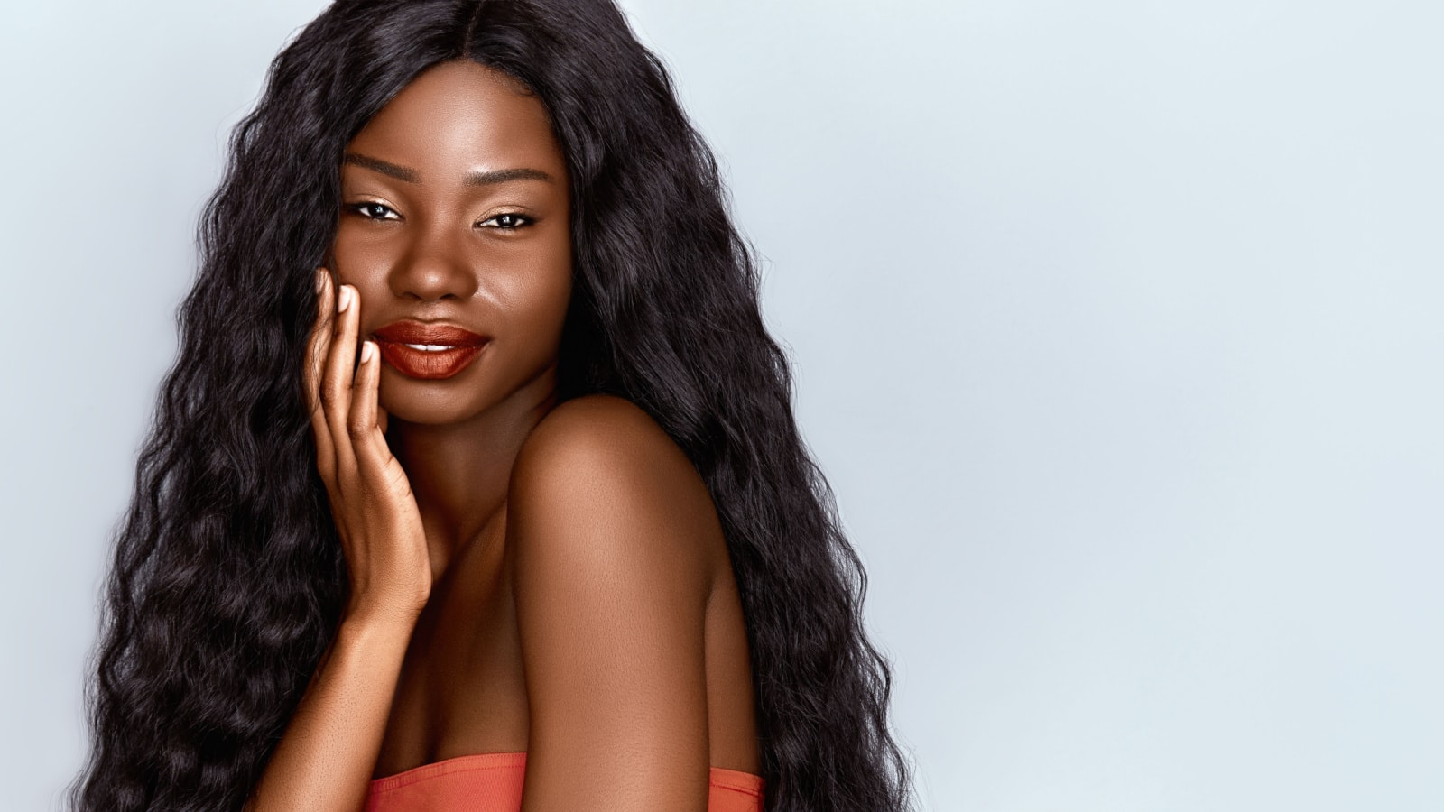 Beautiful African woman portrait. Brunette curly haired young model with dark skin touching her chin and posing against grey background . Web banner witch copy space.