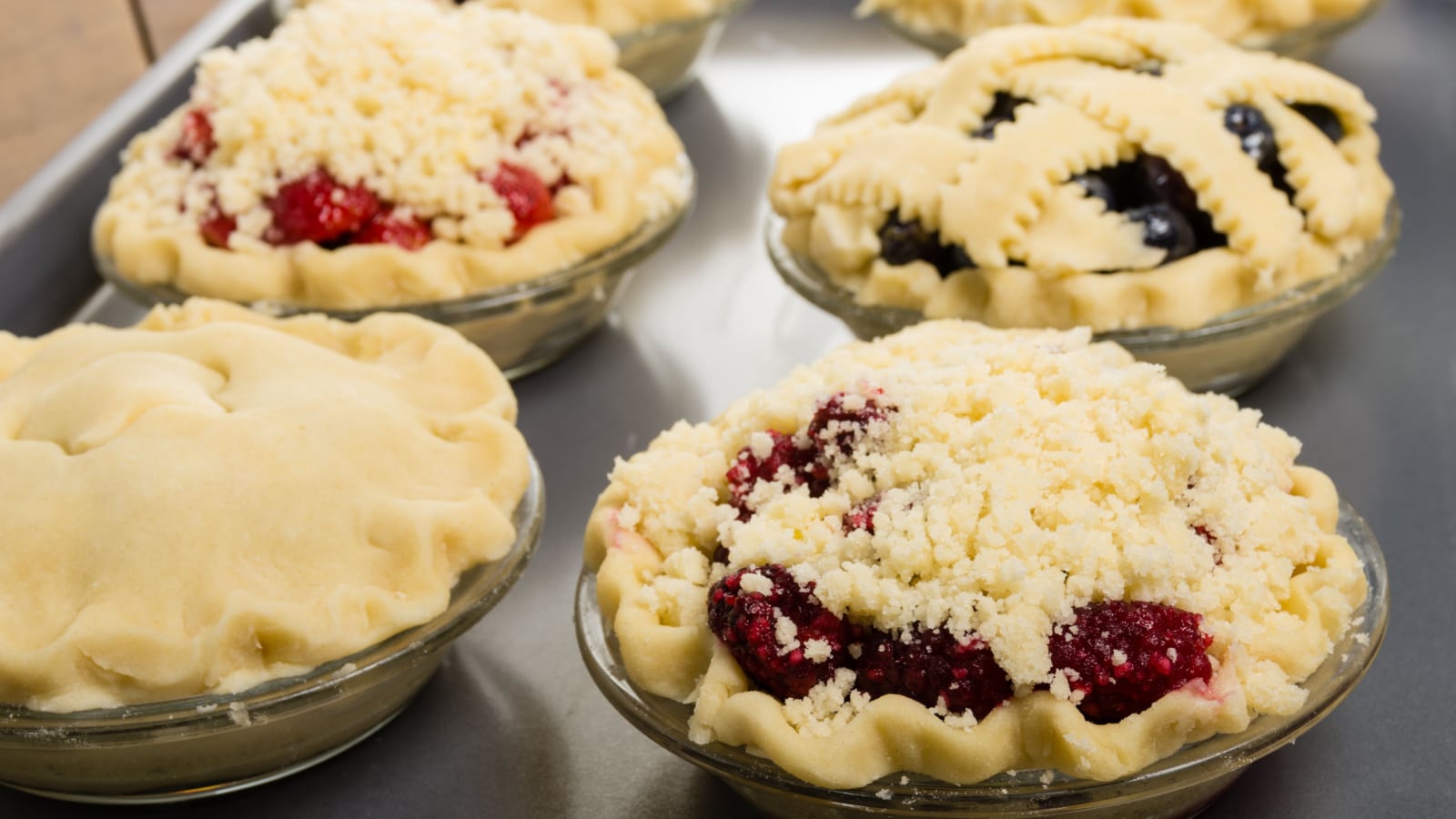 Six homemade fresh fruit pies on a tray made with strawberries raspberries blueberries blackberries