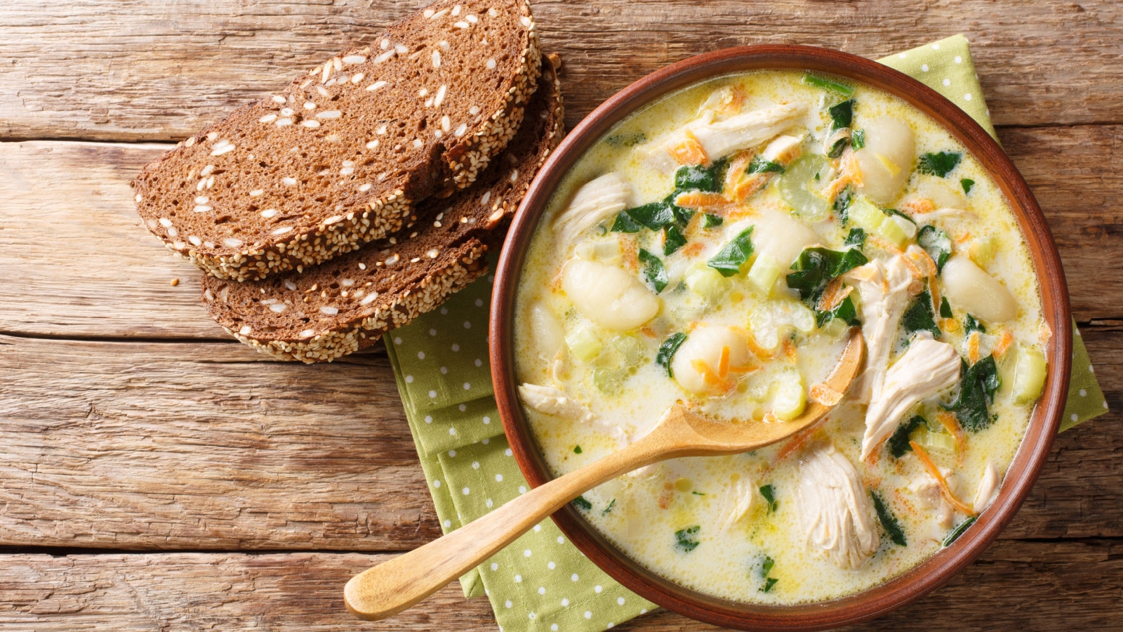 Homemade Italian cream soup with gnocchi, chicken and spinach served with bread close-up in a bowl on the table. Horizontal top view from above