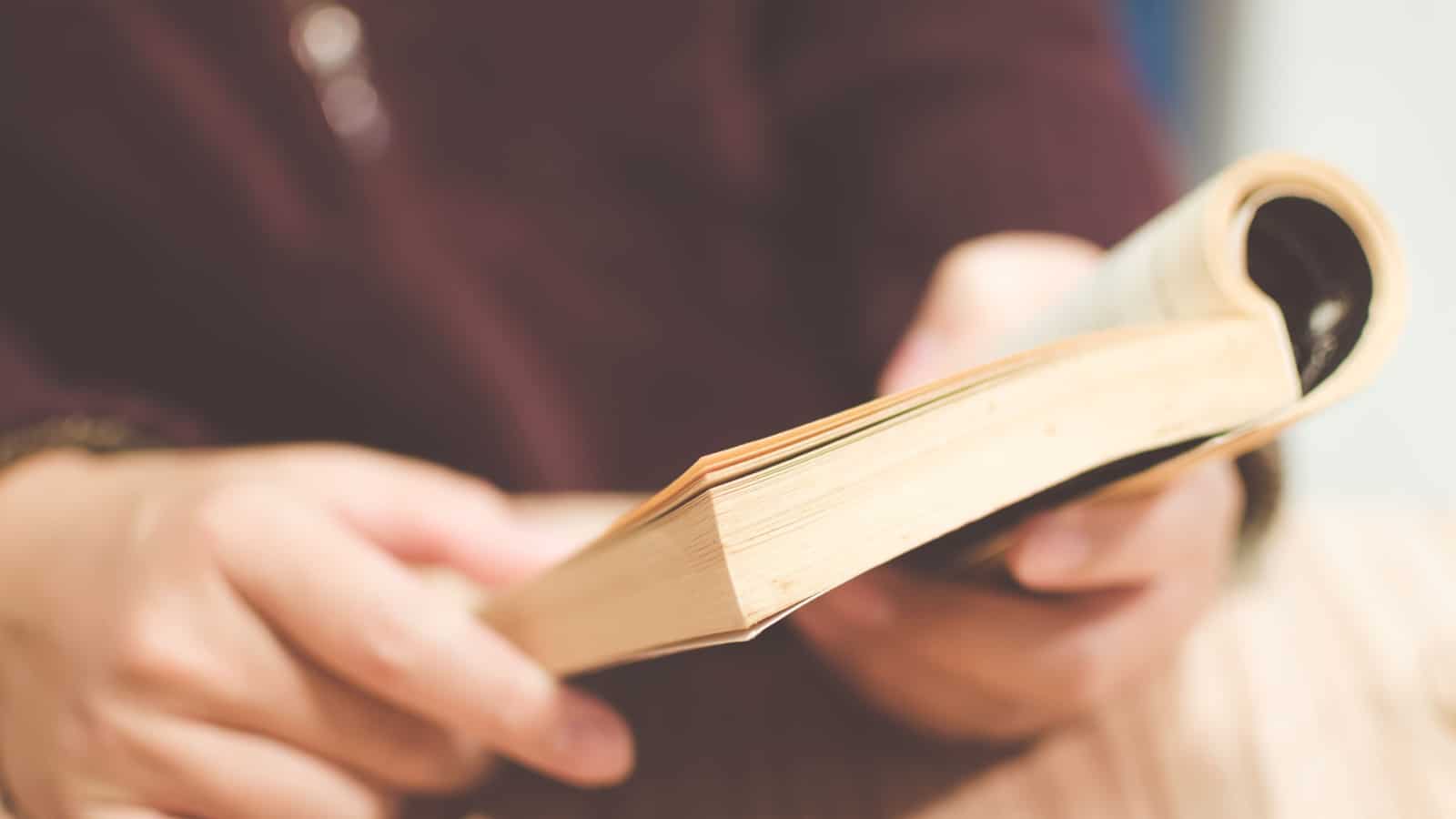 A man reading, holding an old book on his hands. Selective focus. Toned image.