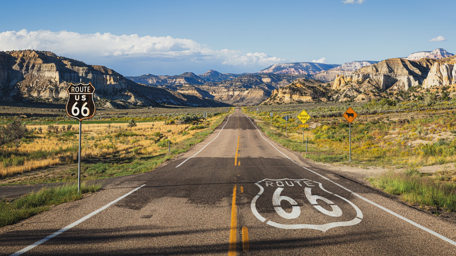 Scenic panoramic view of long straight road on famous Route 66 with historical street signs and paintings in classic american wild western mountain scenery in beautiful golden evening light at sunset