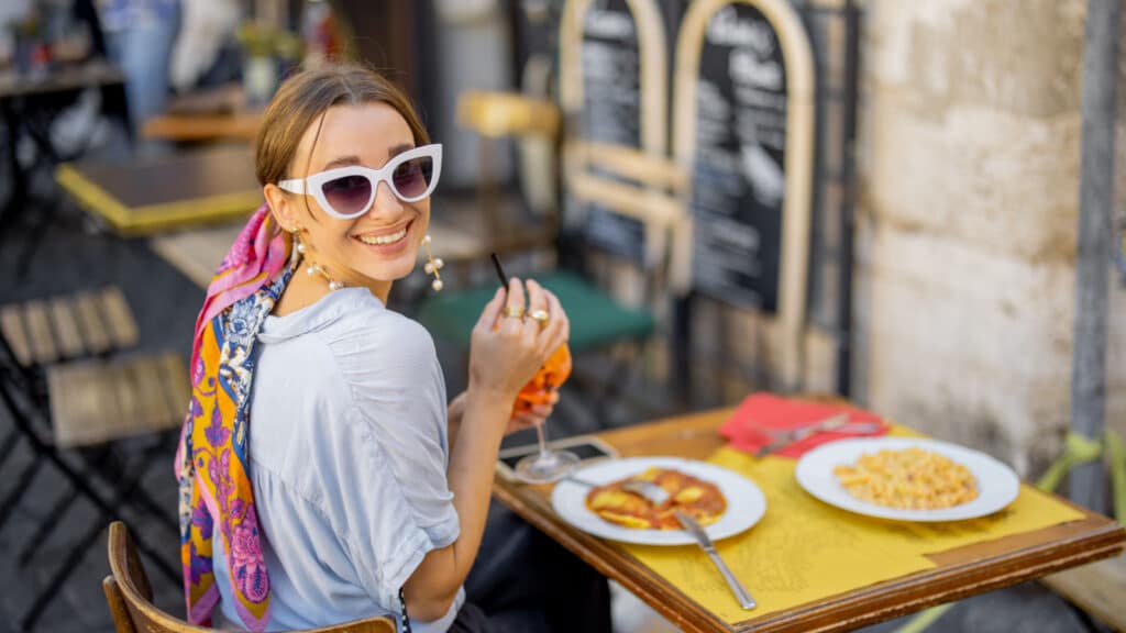 Woman eating italian pasta and drinking wine at restaurant on the street in Rome. Concept of Italian gastronomy and travel. Stylish woman with sunglasses and colorful hair shawl