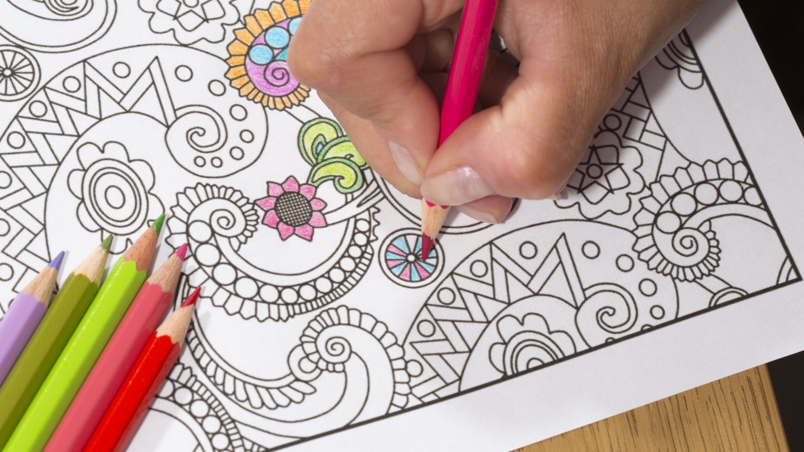 An image of a new trendy thing called adults coloring book. In this image a person is coloring an illustrative and detailed pattern for stress relieve for adults.