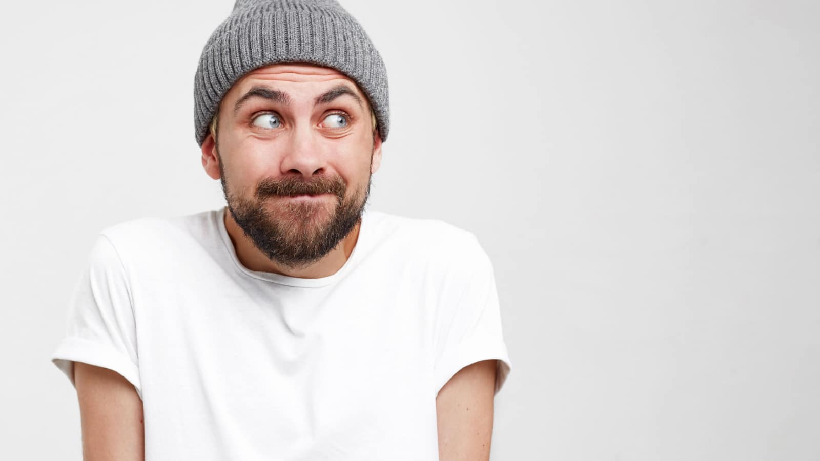 Headshot of a young man with a beard, pressed his head into shoulders and looked away to the side, making excuses or verbally defending himself, puzzled and apologizing, as if saying: “It was not me.”