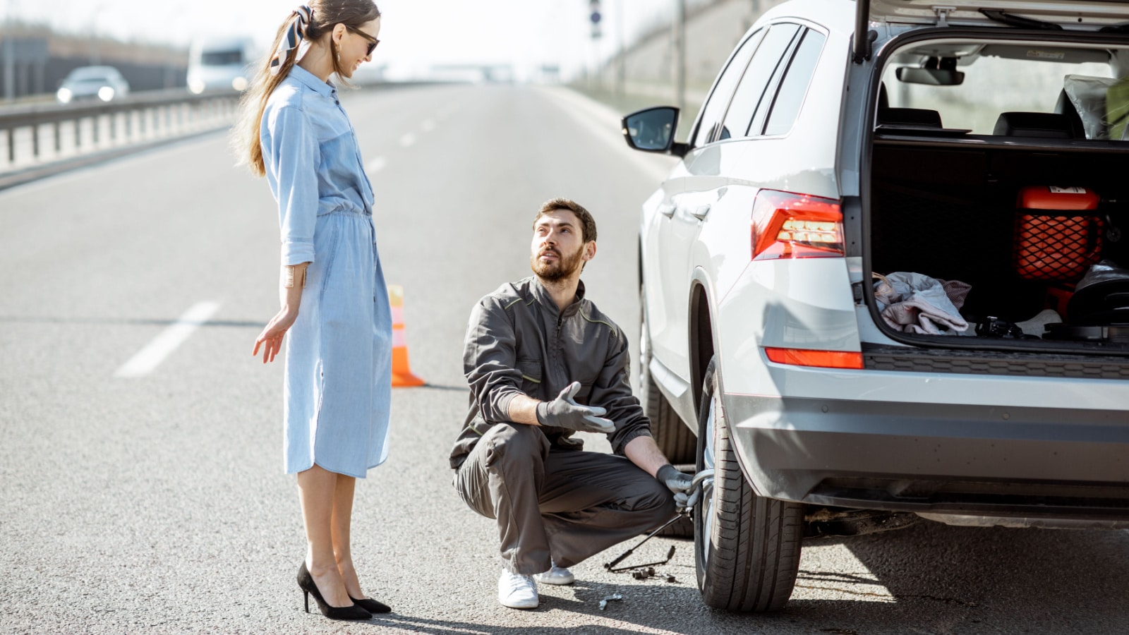 Road assistance worker helping young woman to change a car wheel on the highway